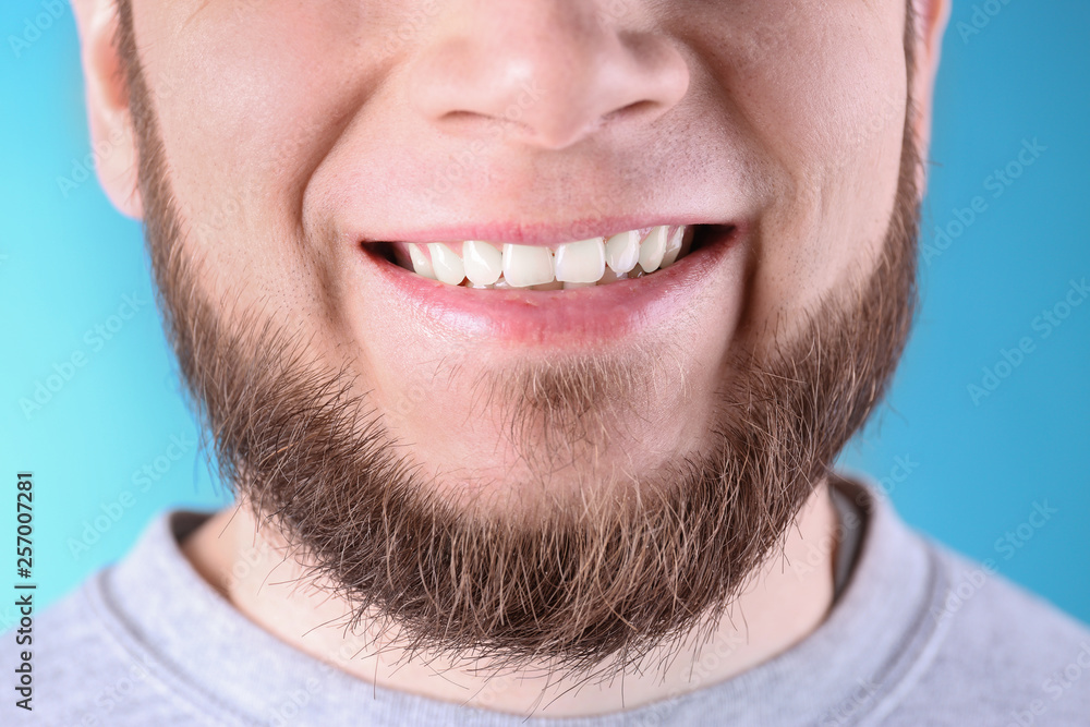 Fototapeta premium Young man with healthy teeth and beautiful smile on color background, closeup