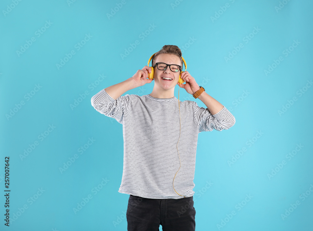 Handsome teenage boy in glasses with headphones on color background Handsome teenage boy in glasses with headphones on color background