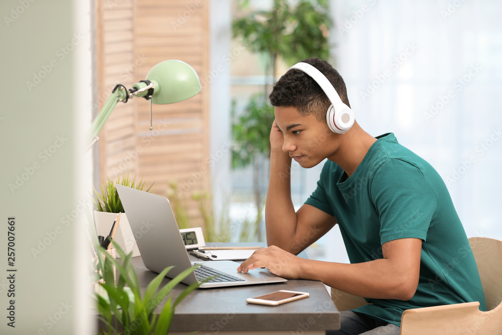 © New Africa - African-American teenage boy with headphones using laptop at table in room