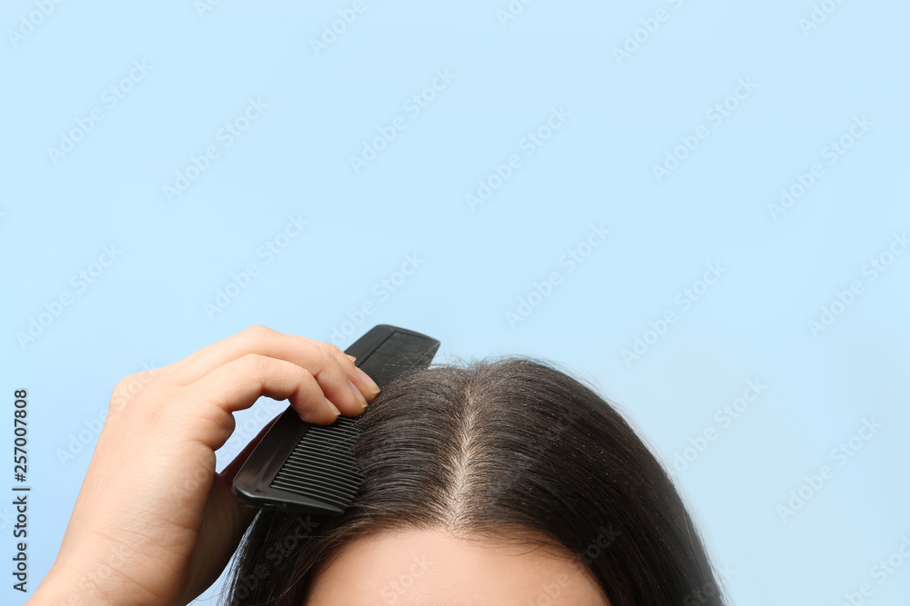 Fototapeta premium Woman with comb and dandruff in her dark hair on color background, closeup. Space for text