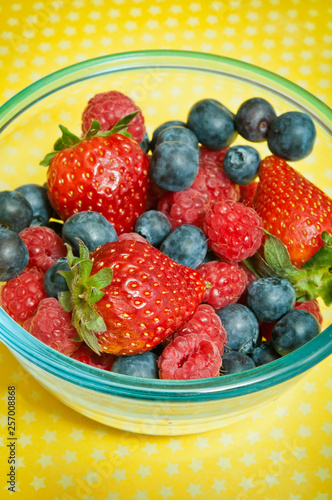 blueberries  strawberries and raspberries in a bowl over yellow background like summer fruit berries concept with various fruit 