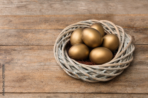 Golden eggs in nest on wooden background, space for text