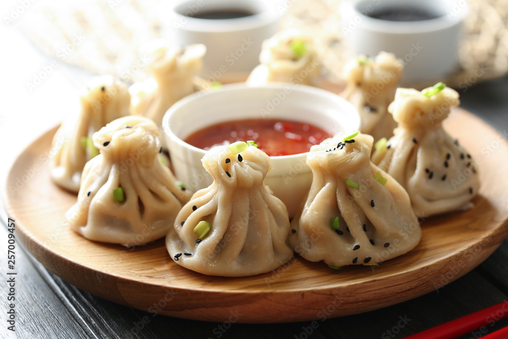 Wooden plate with tasty baozi dumplings and sauce on table, closeup Wooden plate with tasty baozi dumplings and sauce on table, closeup
