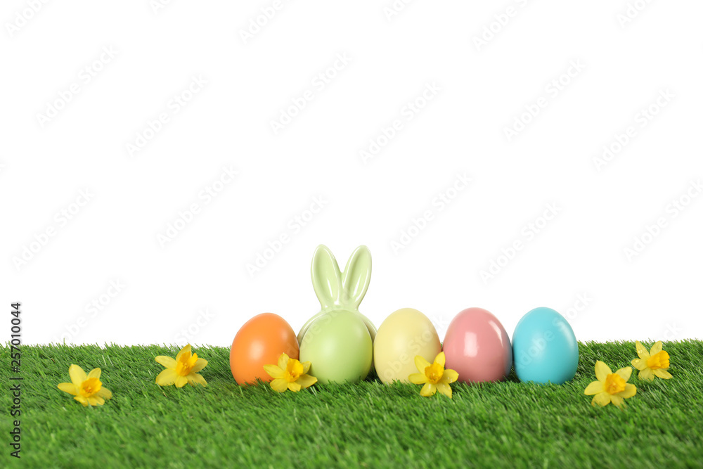 Fototapeta premium Dyed Easter eggs and bunny ears on green grass against white background