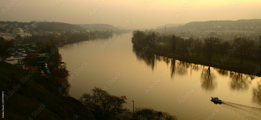 Vltava River at sunset with reflection of trees in Prague