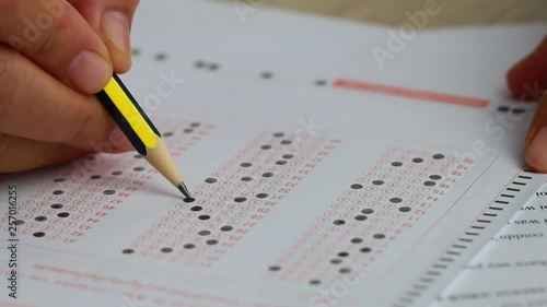 School or university students hands taking exams, writing examination room with holding pencil on optical form answers paper sheet on desk doing final test in classroom. Education assessment Concept photo