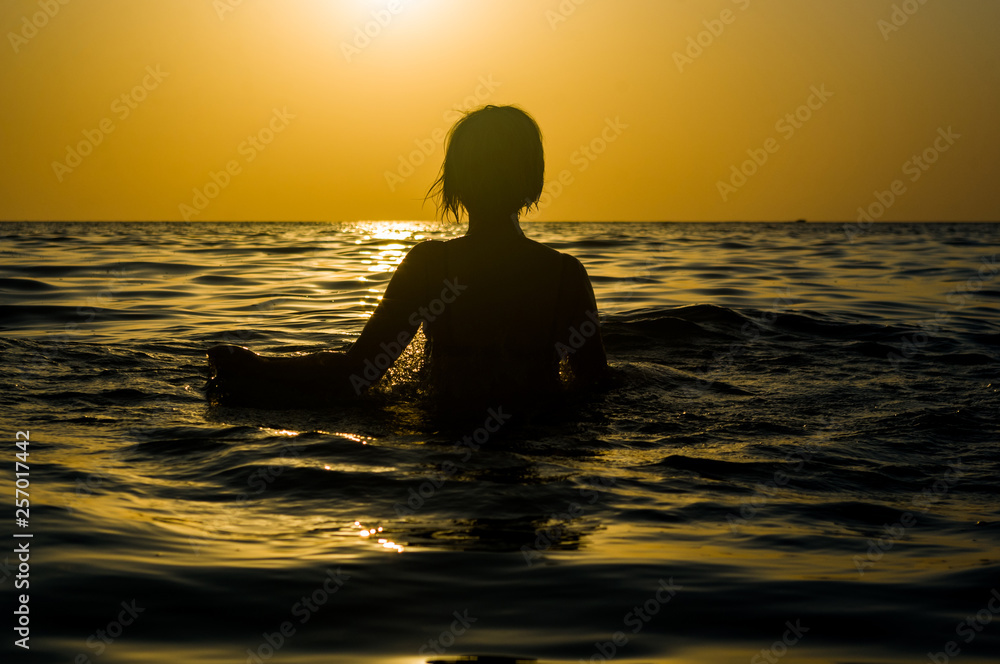 Girl swimming in the sea at sunset, splashes of transparency water, female black silhouette