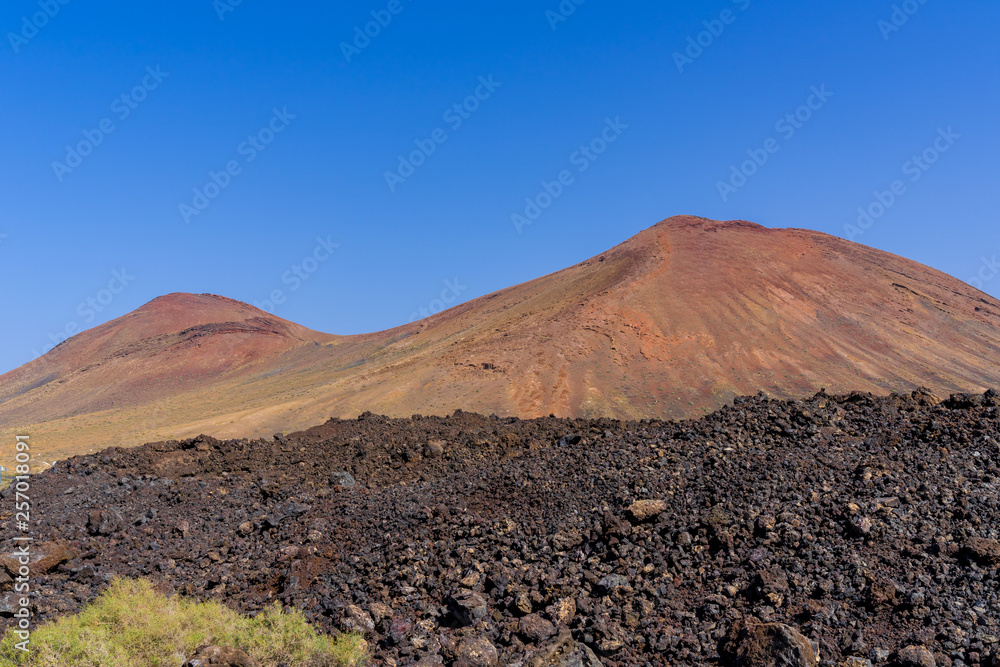 Spain, Lanzarote, Two red mountains of volcanic origin behind black lava field