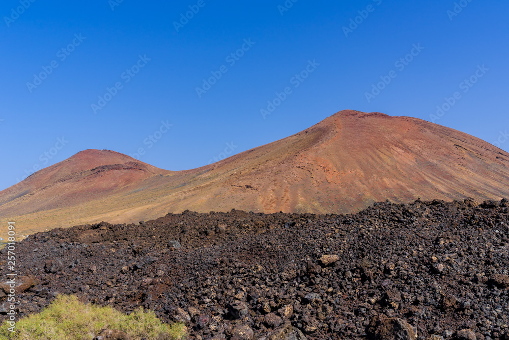 Spain, Lanzarote, Two red mountains of volcanic origin behind black lava field Spain, Lanzarote, Two red mountains of volcanic origin behind black lava field