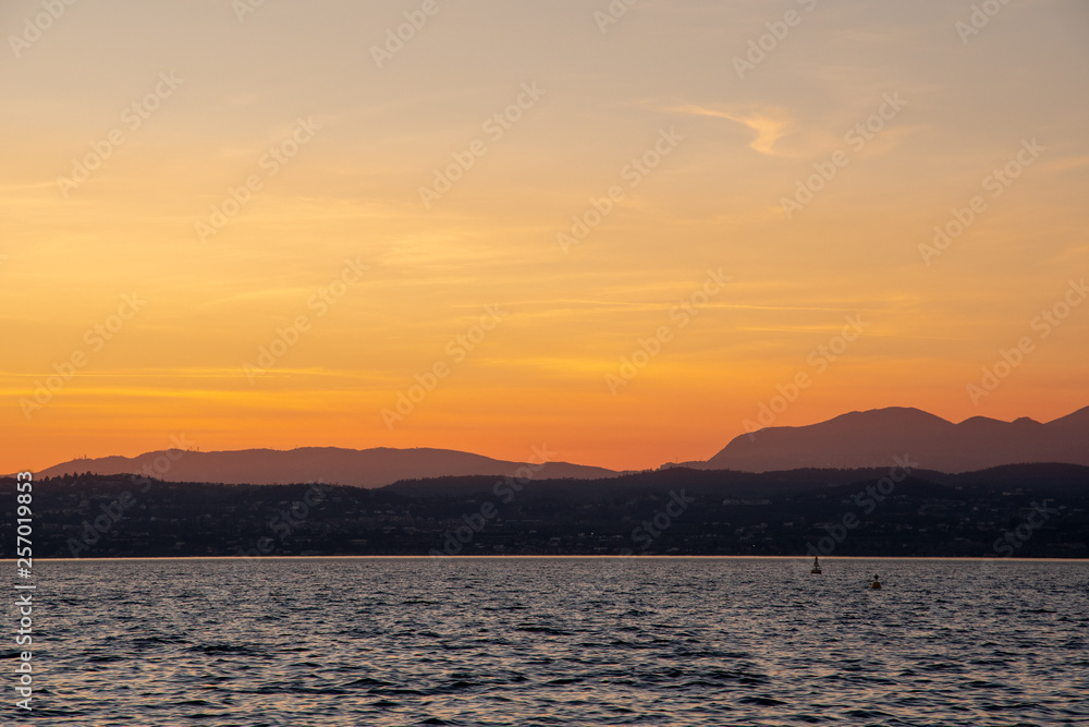 Sunset on Lake Garda with orange sky and coast on the horizon, Sirmione, Lombardy, Italy Sunset on Lake Garda with orange sky and coast on the horizon, Sirmione, Lombardy, Italy