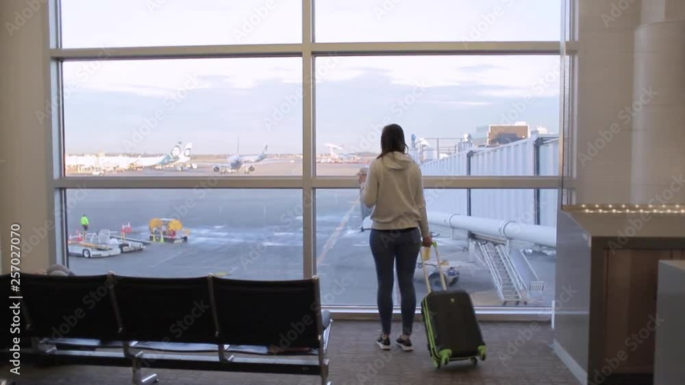 Travel tourist standing with luggage watching at airport window and drink coffee Travel tourist standing with luggage watching at airport window and drink coffee