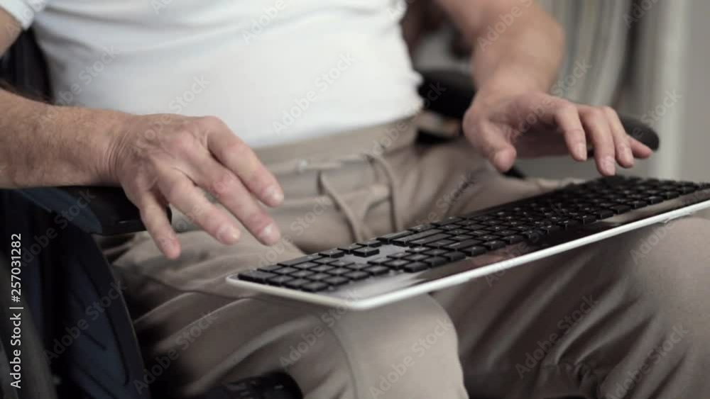An Adult Male in a Wheelchair is Holding a Keyboard While Typing a Letter. An Adult Male in a Wheelchair is Holding a Keyboard While Typing a Letter.