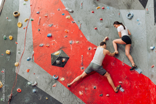 Φωτογραφία Young instructor man putting woman's foot on the climbing wall
