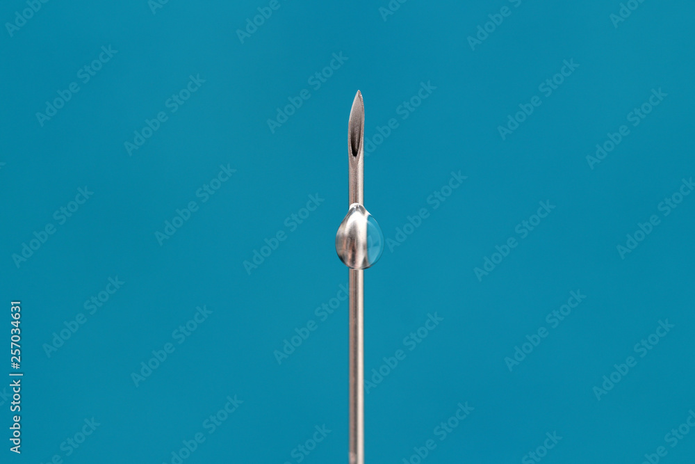 needle of a medical syringe with medicine on a blue background