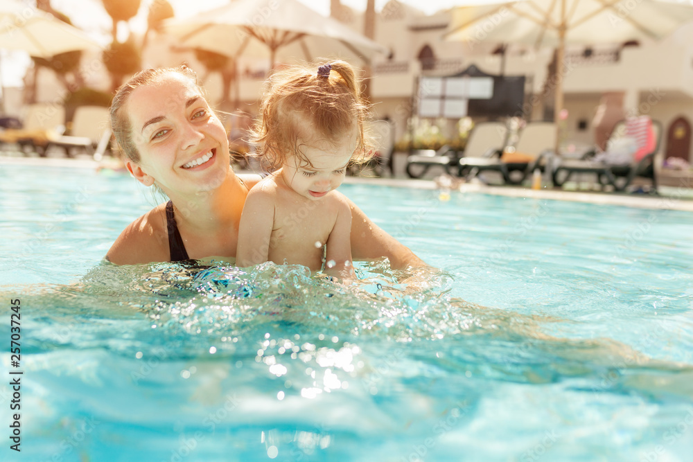 Mom and little daughter are played in the open swimming pool. Family with one child on vacation in warm countries. Positive people on vacation.