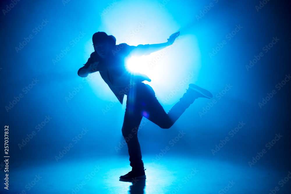 A dark silhouette of a singer on the stage, dancing alone during performance on dark blue neon background with smoke and lights. A dark silhouette of a singer on the stage, dancing alone during performance on dark blue neon background with smoke and lights.