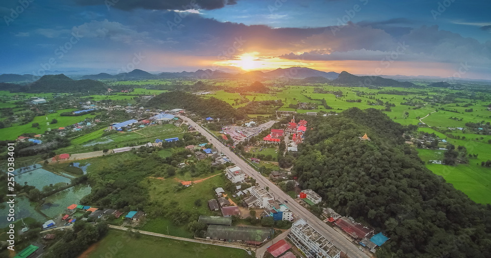 Aerial view sunset above Wat Khao Chong Pran or Bat Temple around with green rice fields, mountains and cloudy sky background, Bat Temple, Ratchaburi, Thailand.