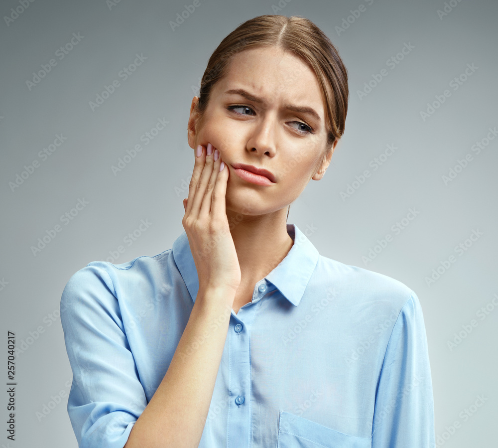 Woman suffering from annoying strong teeth pain. Photo of american woman in blue shirt on gray background. Medical concept Woman suffering from annoying strong teeth pain. Photo of american woman in blue shirt on gray background. Medical concept