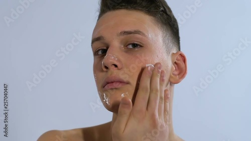 Man applying moisturizing cream on face and smiling, home spa treatment skincare photo