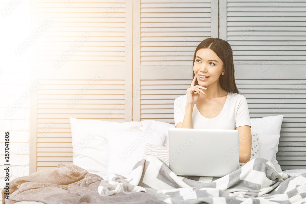 Happy casual beautiful woman working on a laptop sitting on the bed in the house. Happy casual beautiful woman working on a laptop sitting on the bed in the house.