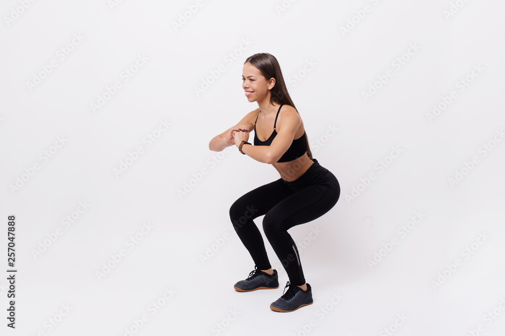 Image of sporty athletic woman in sneakers and tracksuit squatting doing sit-ups in gym isolated over white background