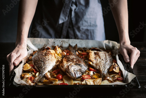 Canvas Print fish for dinner. in female hands baked fish on a baking sheet.