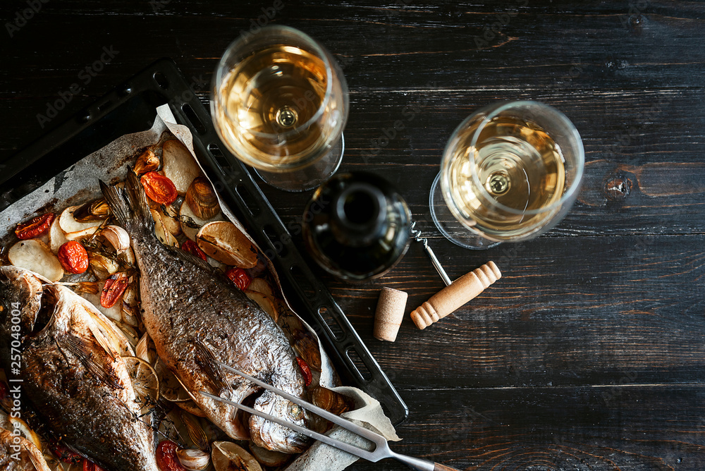 dinner concept for two. two glasses of white wine, baked fish.