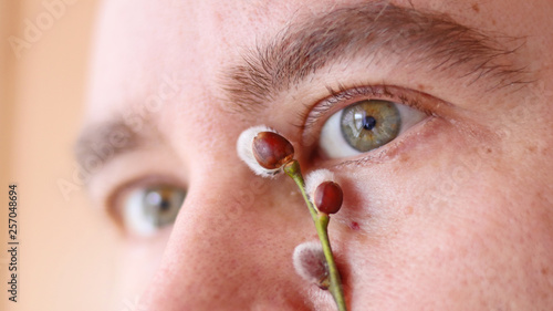 closeup portrait of young man. men's eyes and willow buds. Palm Sunday concept