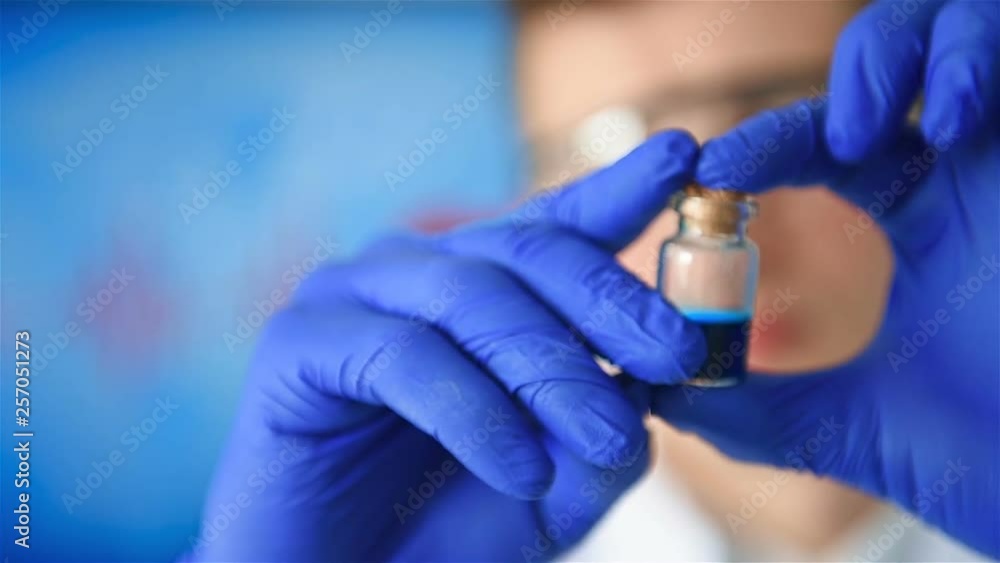 Young Scientist In Gloves And Protective Glasses Holding Blue Tests In Hand. Slow Motion Effect. Young Scientist In Gloves And Protective Glasses Holding Blue Tests In Hand. Slow Motion Effect.