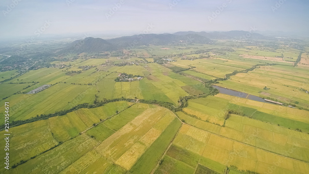 Aerial view above green rice fields plantations with small hill with blue sky background, khao Phra - khao Noi, Thamaka District, Kanchanaburi, Thailand.