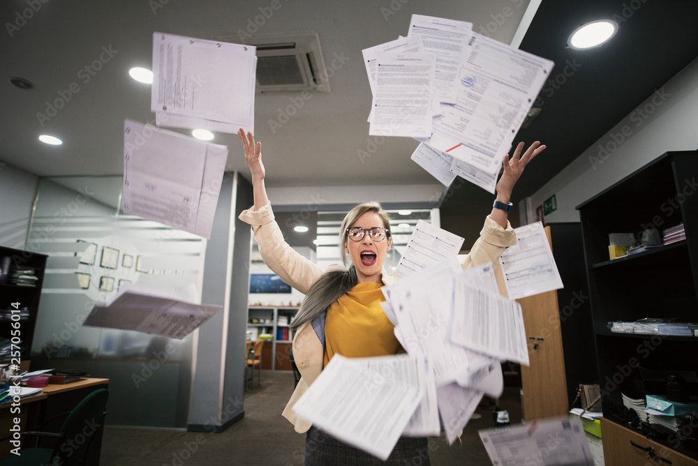 Stressed woman throws papers in the office in an image of relief - obrazy, fototapety, plakaty 
