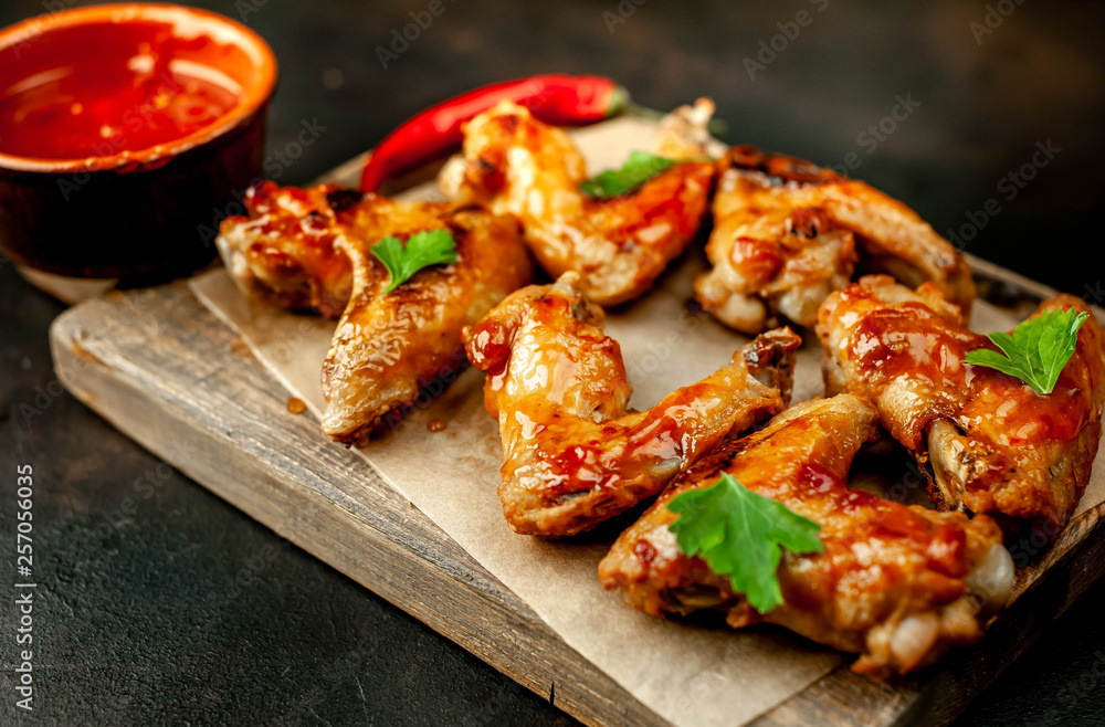 Grilled chicken wings in a barbecue sauce with parsley on a cutting board on a concrete table.