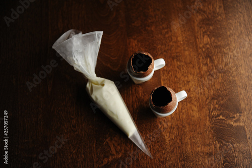 Easter dessert, cooking process. Opened chocolate eggs. Cream in a pastry bag. Dark background. Top view
