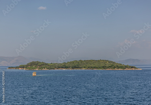 View of a small green islet, in the middle of a beautiful landscape and a calm sea