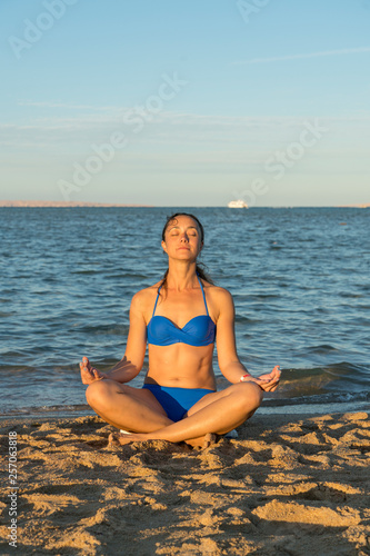Young woman rests on the beach on a hot summer day. Young attractive smiling woman practicing yoga on a sea. Healthy active lifestyle concept