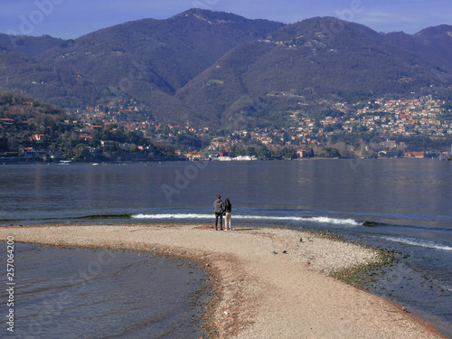 a young couple observes the beauty of the lake from a sand spit. Como - Italy