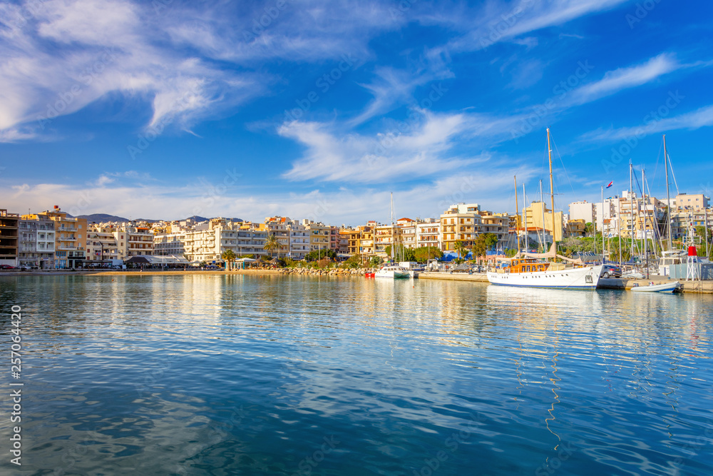 Marina with anchored fishing boats, sandy beach and the beautiful town of Agios Nikolaos at the background, Crete, Greece.