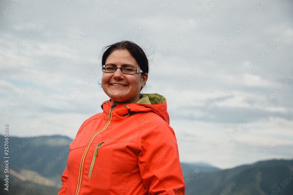 Girl smiling in a red jacket sitting on the mountain. Enjoys the beautiful view around. Girl smiling in a red jacket sitting on the mountain. Enjoys the beautiful view around.