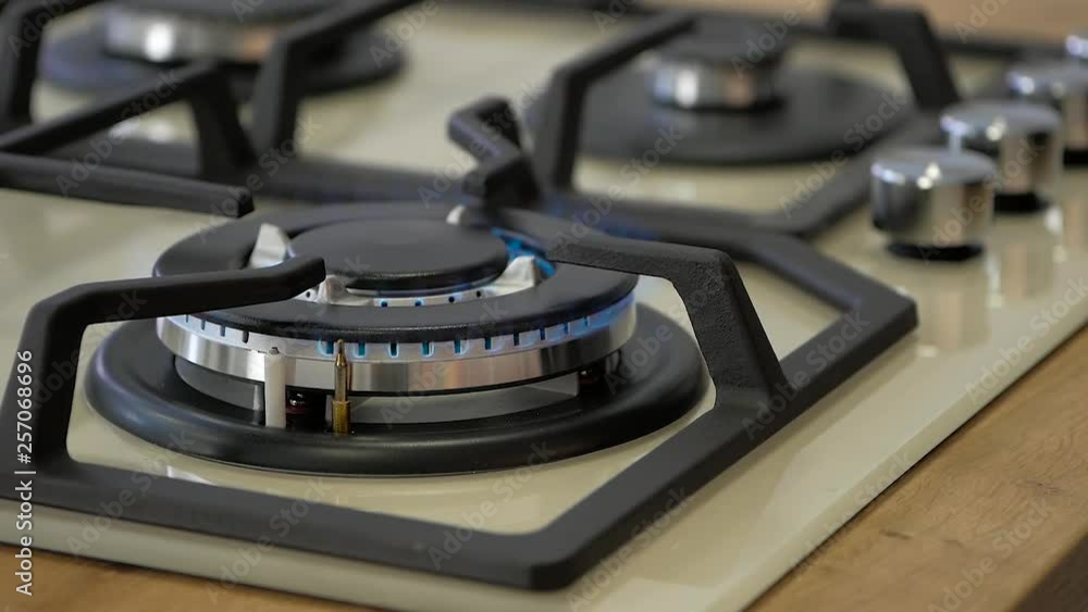 Woman hand turns on new kitchen cooktop gas burner and natural gas ignites burns with blue flame and then turned off. Woman hand turns on new kitchen cooktop gas burner and natural gas ignites burns with blue flame and then turned off.