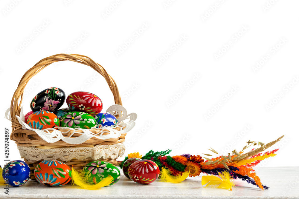 Colorful eggs in basket on white, wooden table. Easter background with eggs, feathers and easter palm.