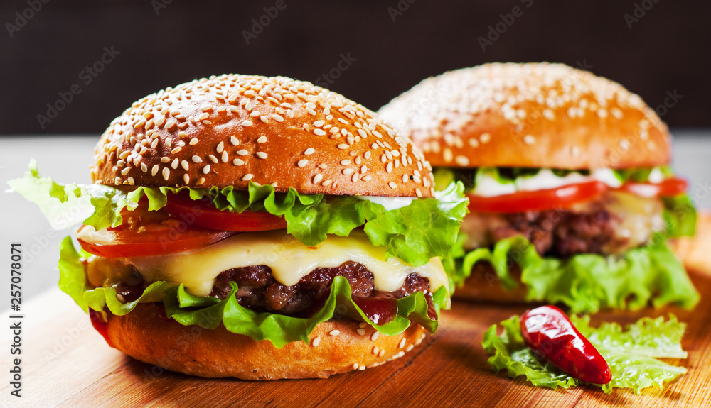 two burger with meat, cheese and vegetables on wooden board two burger with meat, cheese and vegetables on wooden board