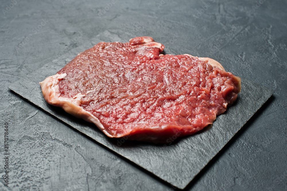 Beef flank steak on a stone Board. Black background, top view, space for text