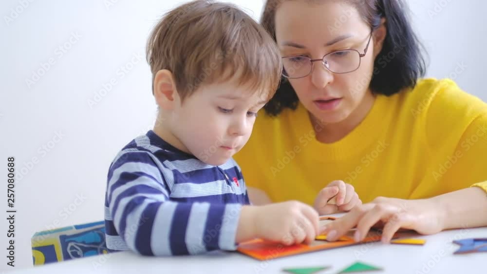 little asian boy collects puzzles with mom sitting at the desk. A cute child collects a picture from large multi-colored details. slow motion. Teacher playing with boy in montessori class little asian boy collects puzzles with mom sitting at the desk. A cute child collects a picture from large multi-colored details. slow motion. Teacher playing with boy in montessori class