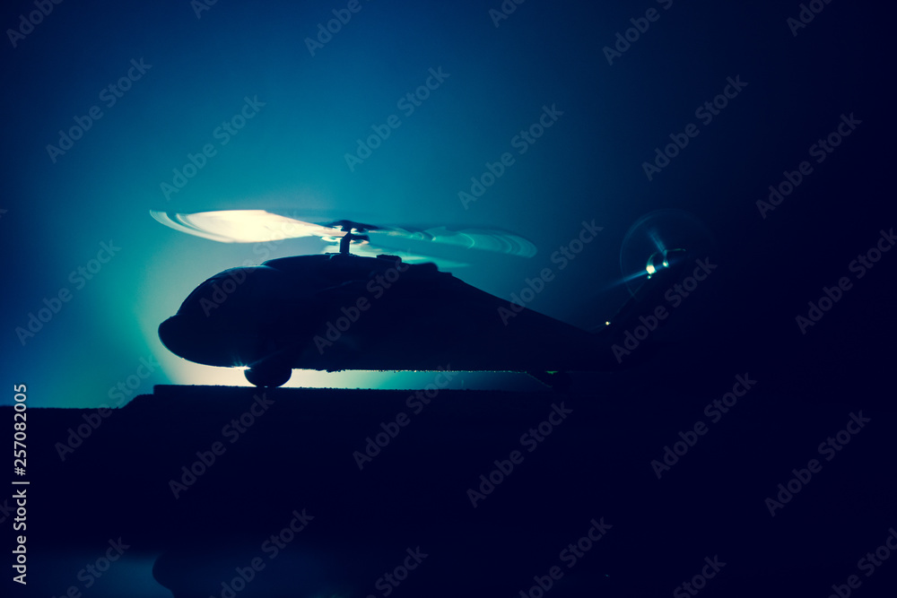 Silhouette of military helicopter ready to fly from conflict zone. Decorated night footage with helicopter starting in desert with foggy toned backlit. Selective focus. Silhouette of military helicopter ready to fly from conflict zone. Decorated night footage with helicopter starting in desert with foggy toned backlit. Selective focus.