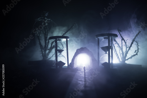 Time concept. Silhouette of a man standing between hourglasses with smoke and lights on a dark background. Surreal decorated picture