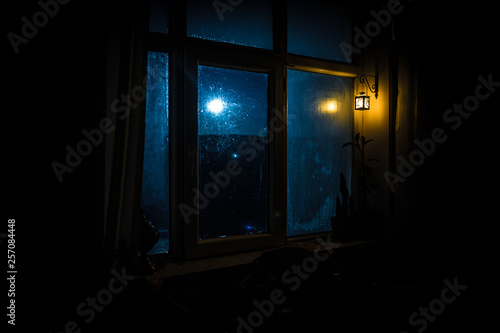 Night scene of stars seen through the window from dark room. Night sky inside dark room viewing from window with old vintage lantern. Long exposure shot
