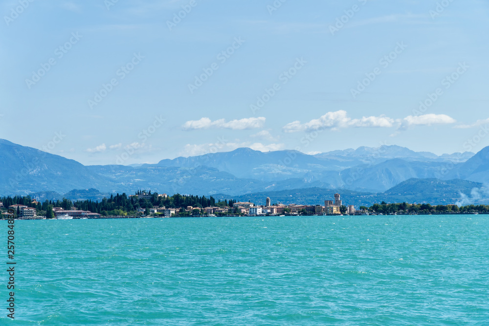Panoramic view of Sirmione from Garda Lake with mountains in the background. Sirmione is medieval town located on the Sirmio peninsula of Lake Garda, Italy, Europe.