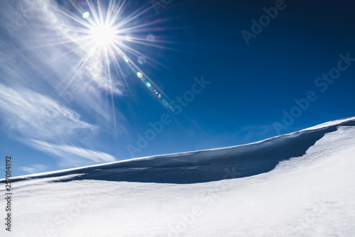 Diagonal edge of a snowy slope and the sun on a clear sky © Elza_R