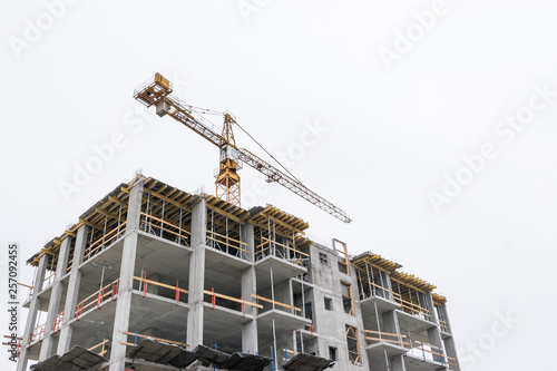 High-rise building crane with a long arrow of yellow color against the sky above a concrete building under construction with brick walls © Тарас Квакуш