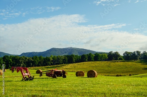 Green grass field with grass bundles, blue sky, rolling hills, farm equipment